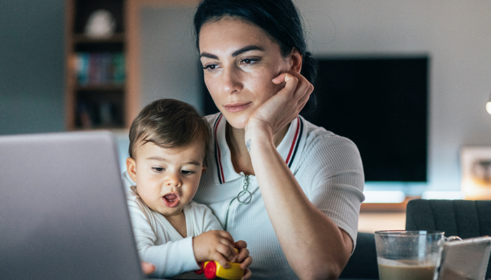 Parent using laptop while holding a child.